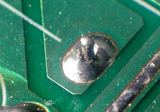 Macro photo of a cold solder joint showing a dull, balled joint on a green PCB