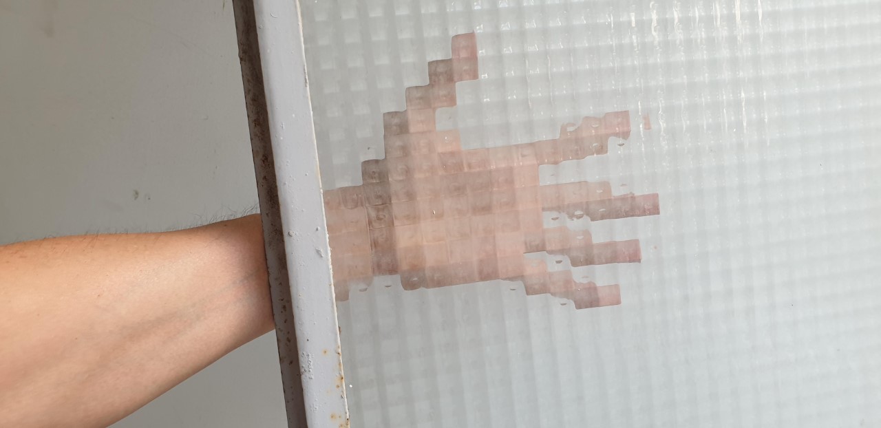 A real arm reaching behind a window made of privacy glass, sampling the analog scene into blocks